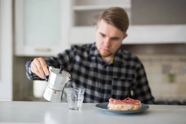 Conceito de pessoas, café da manhã e bebidas - jovem barbudo bonito está bebendo café na cozinha — Fotografia de Stock
