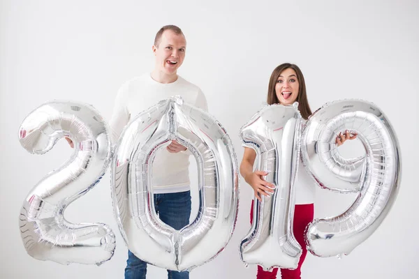 Conceito de ano novo, celebração e feriados - Sinal de posse de casal de amor surpreso 2019 feito de balões de prata para o ano novo no fundo da sala branca — Fotografia de Stock