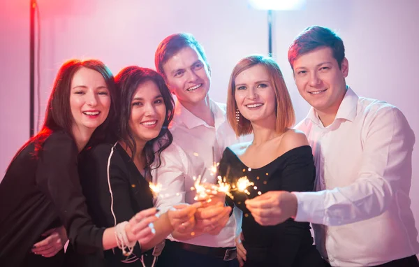 Fiesta de año nuevo, la celebración y el concepto de días festivos - Jóvenes hombres y mujeres alegres celebración de bengalas ardientes —  Fotos de Stock