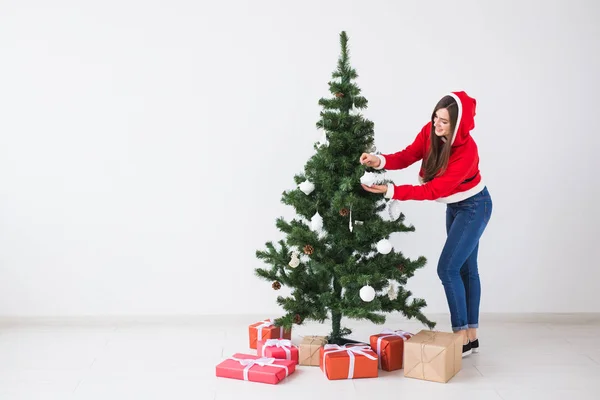 Férias de inverno, xmas e conceito de pessoas - Jovem feliz vestida com traje de Papai Noel decorando árvore de Natal em branco o quarto com espaço de cópia — Fotografia de Stock