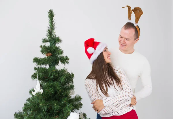 Lustiges Liebespaar in der Nähe von Weihnachtsbaum. Mann trägt Hirschhörner und Frau Weihnachtsmütze — Stockfoto