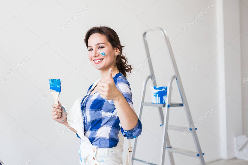 Repair, renovation and people concept - young woman painting the wall and looks like very happy, she showing thumb up