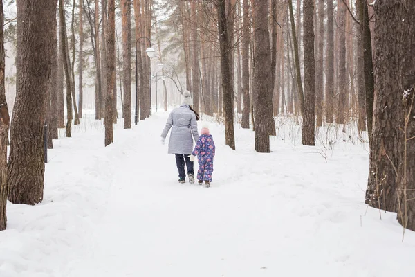Inverno, família e conceito de pessoas - Mãe está andando com sua filhinha no parque nevado, vista para trás — Fotografia de Stock