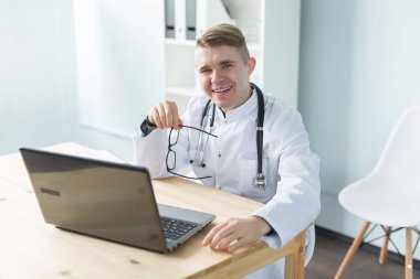 Tıp, çalışma ve insan kavramı - Doktor laptop ile masada oturan ve gülümseyen