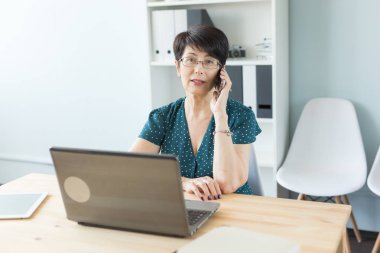 İnsanlar kavramı - ofis ve iş orta yaşlı kadın laptop ile çalışan ve bir telefon görüşmesi ofisinde