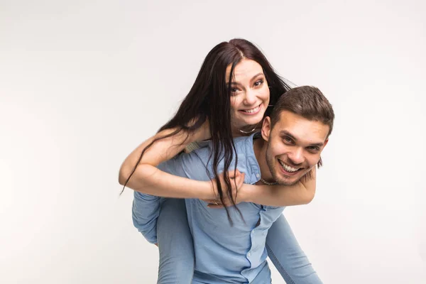 Divertimento e conceito de relacionamento - Homem carregando namorada de costas no fundo branco — Fotografia de Stock