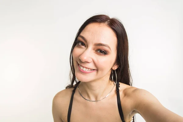 Boldog európai női modell, sötét hajú, beltéri fotózás élvezi. fiatal nő vesz egy selfie fehér háttér — Stock Fotó