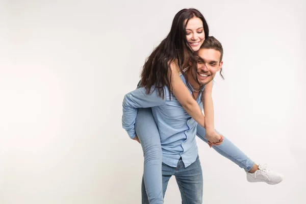 Divertimento e conceito de relacionamento - Homem carregando namorada de costas no fundo branco — Fotografia de Stock