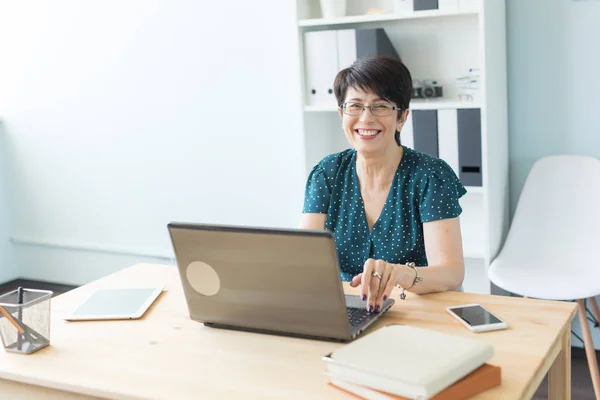 Geschäfts-, Technologie- und Personenkonzept - Frau mittleren Alters bei der Arbeit mit Laptop und Lächeln — Stockfoto