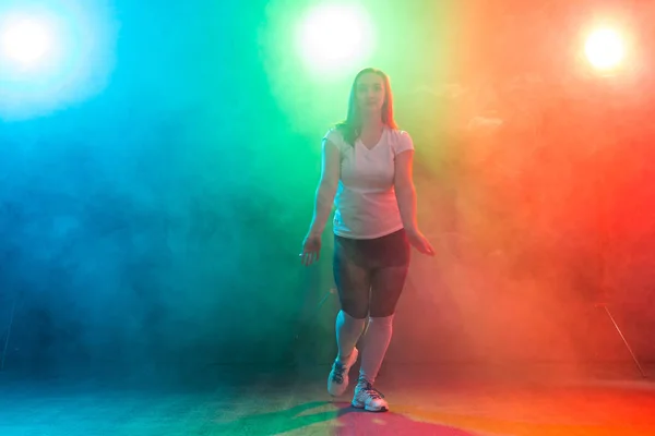 Modern dance, sport and people concept - young woman dancing jazz funk in the darkness under colourful light