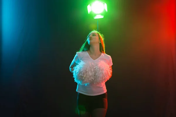 Девушка из группы поддержки танцует с помпонами на цветном фоне — стоковое фото