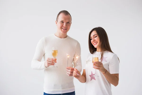 Conceito do Dia dos Namorados - Jovem feliz sorrindo alegre casal atraente celebrando com copos de champanhe e faíscas no fundo branco — Fotografia de Stock