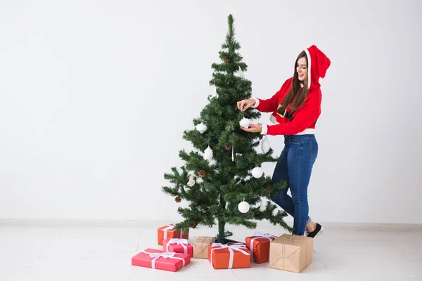 Zimní prázdniny, Vánoce a lidé koncept - krásná mladá žena zdobí vánoční stromeček v bílé místnosti s kopií prostor — Stock fotografie