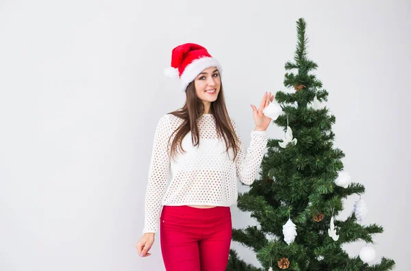 Зимние праздники, Рождество и люди концепция - Портрет красивой молодой женщины в Санта шляпе украшая елку дома — стоковое фото