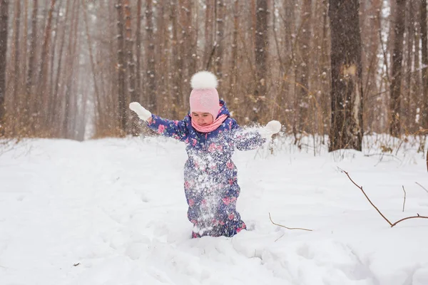 Концепция детства и людей - девочка, гуляющая зимой на свежем воздухе и выбрасывающая снег — стоковое фото