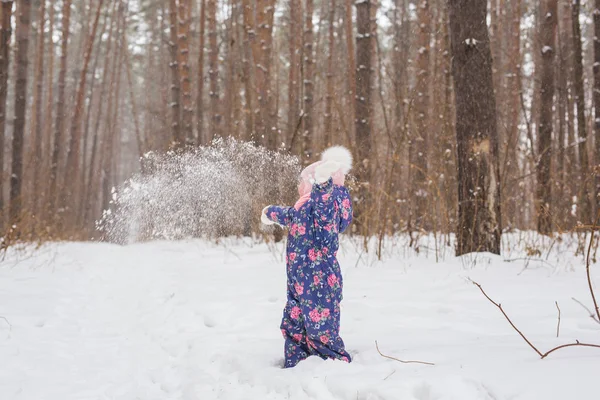 Concepto de la infancia y la gente - niña caminando en el invierno al aire libre y arrojando la nieve — Foto de Stock