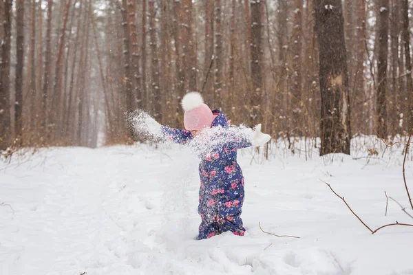 Childhood and people concept - child girl walking in the winter outdoors and throwing the snow up — Stock Photo, Image