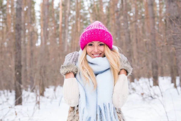 Conceito de moda e pessoas - Retrato de mulher loira jovem atraente vestida com casaco branco e chapéu rosa no parque nevado de inverno — Fotografia de Stock