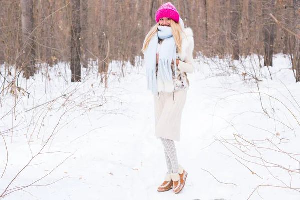 Stagione e concetto di persone - Attraente donna bionda vestita con cappotto bianco e cappello rosa in piedi nel parco innevato invernale — Foto Stock