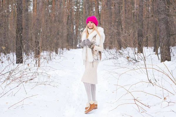 Stagione e concetto di persone - Attraente donna bionda vestita con cappotto bianco e cappello rosa in piedi nel parco innevato invernale — Foto Stock