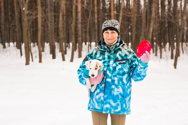 Dono de animais de estimação e conceito de inverno - Mulher de meia-idade brincando com seu cão terrier jack russell no parque nevado . — Fotografia de Stock