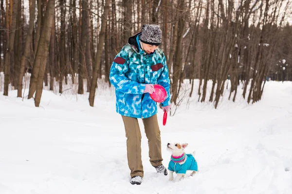 Dono de animais de estimação e conceito de inverno - Mulher de meia-idade brincando com seu cão terrier jack russell no parque nevado . — Fotografia de Stock
