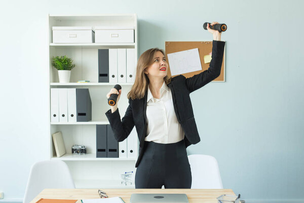 Бизнес, фитнес в офисе и концепции людей - довольная женщина в офисе держа гантель в руке
