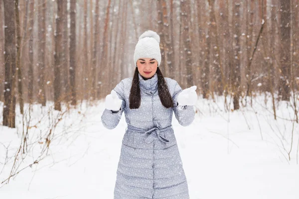 Winter, season and people concept - Woman in grey coat and white hat walking in winter park and playing with snow — Stock Photo, Image