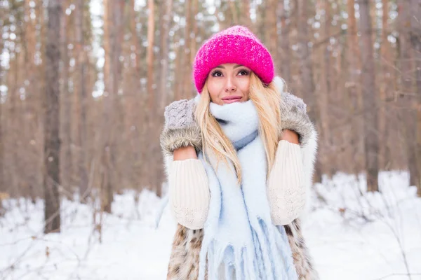 Conceito de moda e pessoas - Retrato de mulher loira jovem atraente vestida com casaco branco e chapéu rosa no parque nevado de inverno — Fotografia de Stock