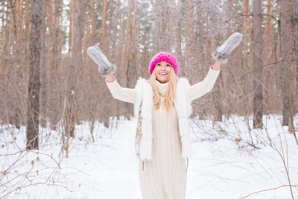 Веселощі, зима і концепція людей - приваблива молода жінка, одягнена в пальто, що кидає сніг . — стокове фото