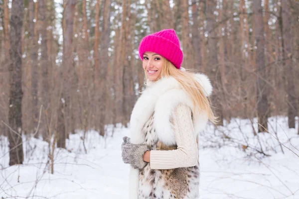 Μόδα, εποχή και άνθρωποι έννοια - ευτυχισμένη γυναίκα ξανθιά σε ένα ροζ καπέλο και γάντια και πουλόβερ μέσα στο δάσος του χειμώνα είναι χαμογελαστός — Φωτογραφία Αρχείου