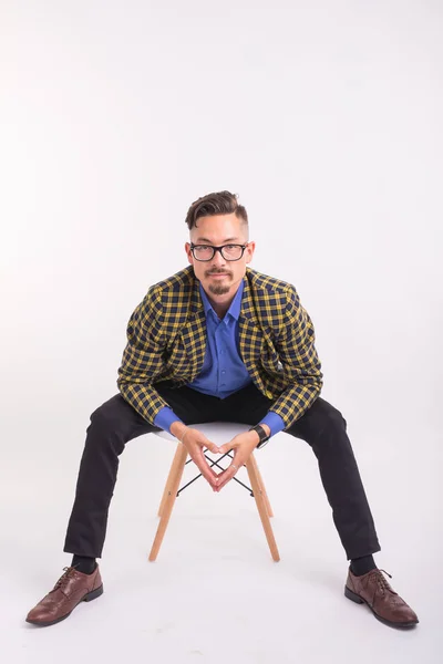 Gente, moda y concepto de belleza - joven guapo sentado en la silla, aislado sobre fondo blanco — Foto de Stock