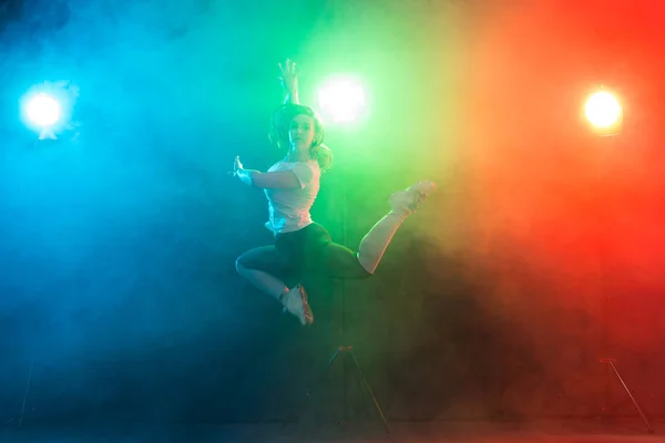 Baile, deporte, jazz funk y el concepto de la gente - mujer joven saltar en la oscuridad bajo una luz colorida — Foto de Stock