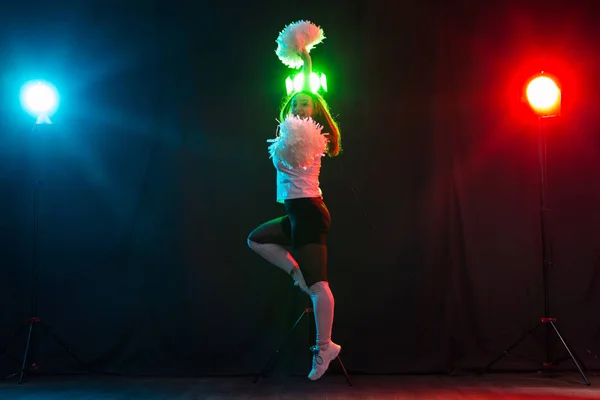 Baile, deporte, hermoso y la gente concepto - joven animadora chica en la oscuridad mostrar pompones y sonrisa — Foto de Stock