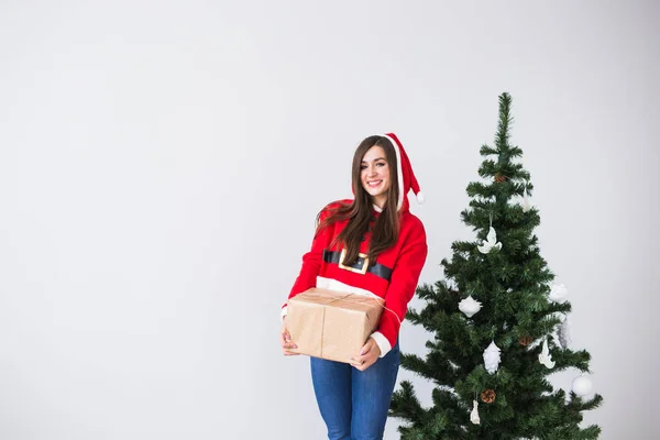 Mladá veselá žena držící krabičky nosí Santa kostým. Vánoční stromeček pozadí s kopií prostor — Stock fotografie