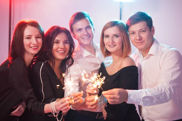 Celebrando con diversión. Grupo de alegres hombres y mujeres jóvenes que llevan bengalas. Año nuevo, vacaciones y concepto de fiesta . —  Fotos de Stock