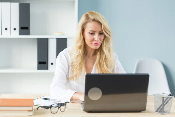Concept de travail, d'affaires, de technologie et de personnes - jeune femme blonde regardant quelque chose à l'écran d'un ordinateur portable et souriant — Photo