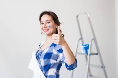 Onarım, yenileme ve insanlar kavramı - genç kadın duvar boyama ve gibi görünüyor çok mutlu o başparmak gösterilmesini