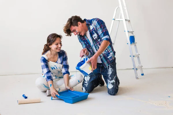 Concept de personnes et d'intérieurs - Jeune couple assis sur le sol blanc et versez de la peinture — Photo