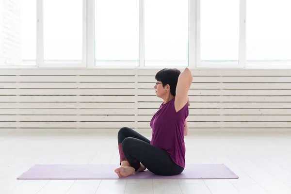 Gente, yoga, deporte y concepto de salud - mujer atractiva estirando las manos sentada en la esterilla de yoga aislada sobre fondo blanco —  Fotos de Stock