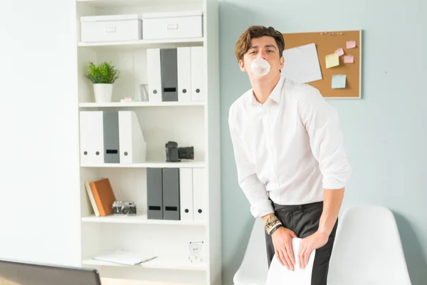 Koncepcja biznesu, rozrywki i żart - młody mężczyzna dmuchanie bańki gumy do żucia w biurze — Zdjęcie stockowe