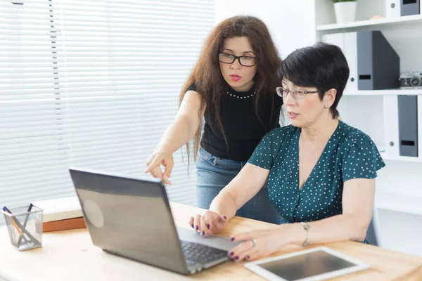 Geschäftsleute, Technologie und Kommunikationskonzept - Frau mittleren Alters zeigt einer anderen Frau am Laptop im Büro etwas — Stockfoto