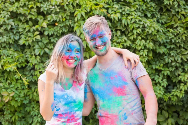 Концепция праздника и людей - Улыбающаяся женщина и мужчина позируют с разноцветным порошком на лицах — стоковое фото