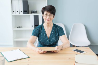 Office, iş, teknoloji ve insan kavramı - güzel orta portre onun el dijital tablet tutarak ve online çalışma ofisinde oturan kadın yaşlı.