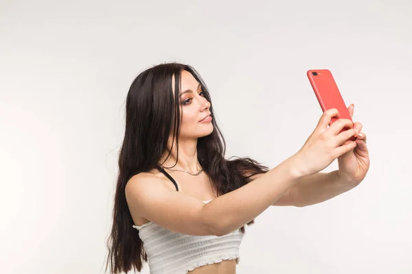 Boldog európai női modell, sötét hajú, beltéri fotózás élvezi. Fiatal nő vesz egy selfie-ra könnyű háttér — Stock Fotó
