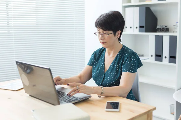 Business, tecnologia e concetto di persone: le donne di mezza età lavorano in ufficio e utilizzano un computer portatile — Foto Stock