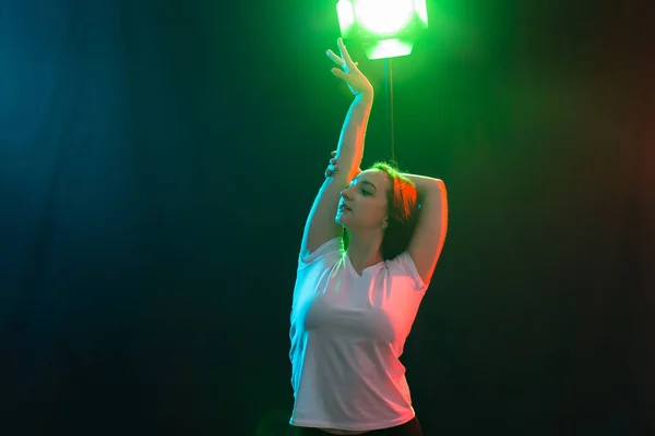 Танцы, рок-н-ролл и хип-хоп концепция - молодая женщина танцует в темноте и сложила руки над головой — стоковое фото