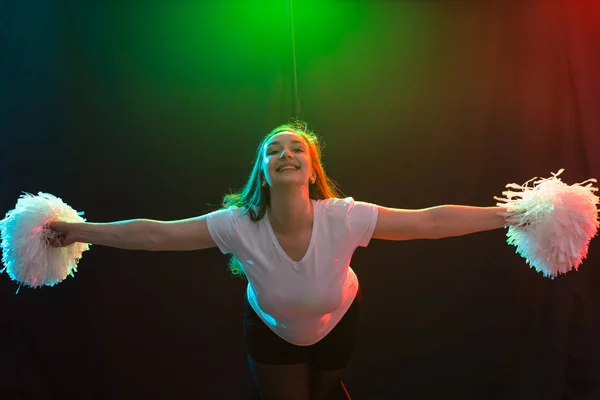 Concepto de danza, deporte y gente: una hermosa joven bailando en la oscuridad con pompones y sonriendo — Foto de Stock