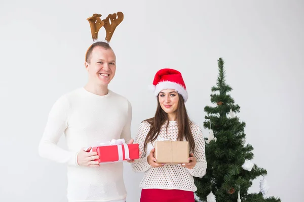 Divertida pareja amorosa cerca del árbol de Navidad. El hombre usa cuernos de ciervo y la mujer usa sombrero de santa — Foto de Stock