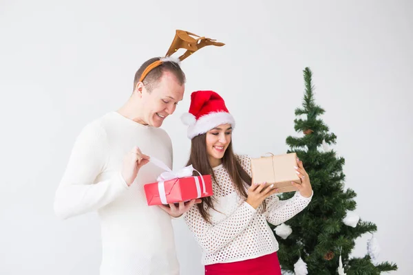 Casal amoroso engraçado perto da árvore de Natal. Homem usa chifres de veado e mulher usa chapéu de Pai Natal — Fotografia de Stock